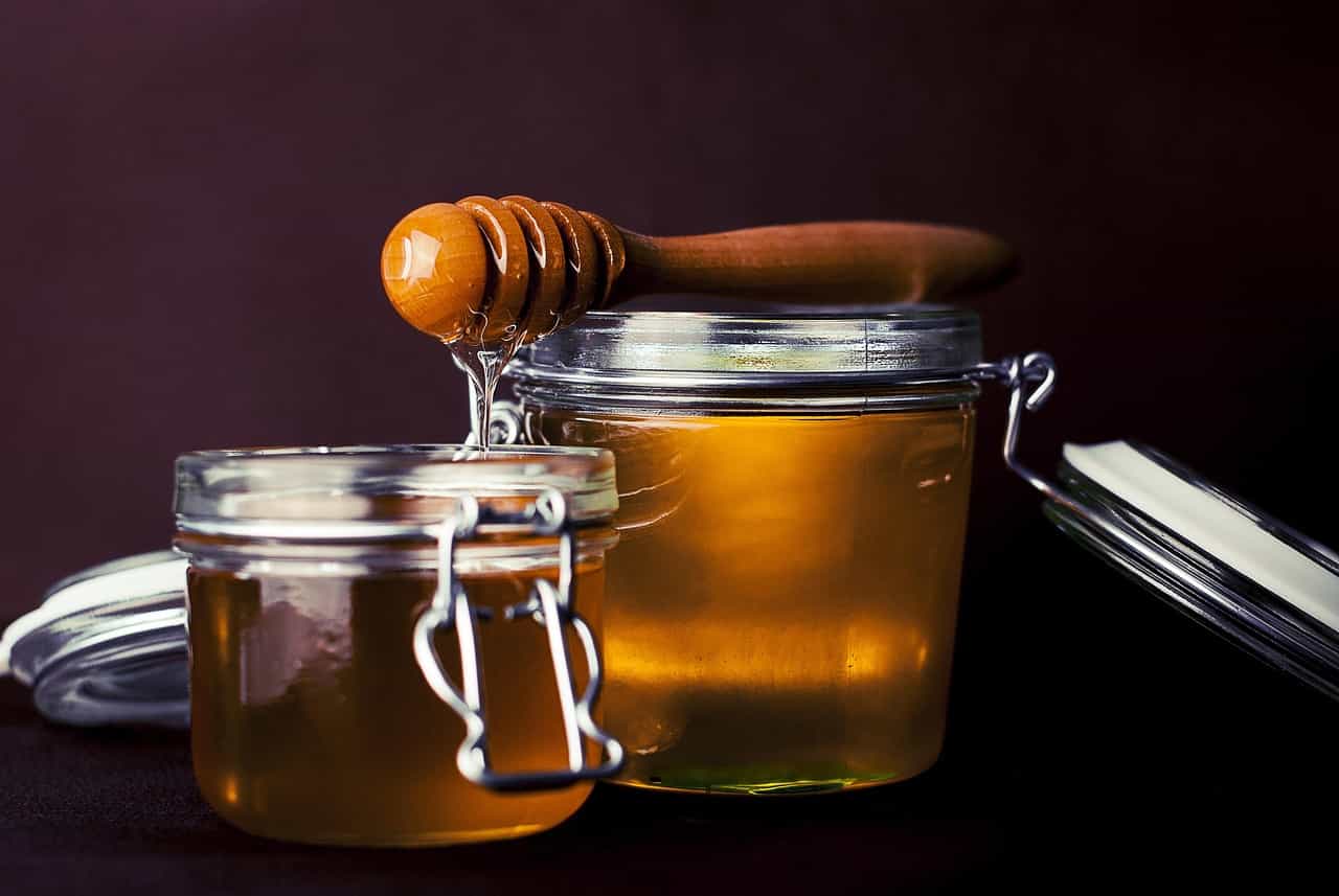 Honey being drizzled from a wooden dipper into glass jars