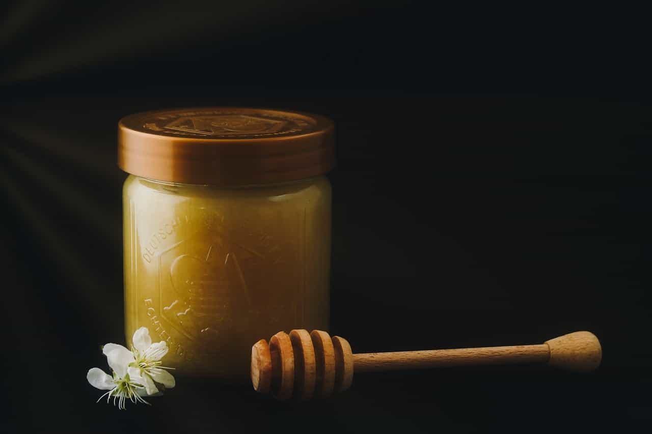 A jar of raw honey with a wooden dipper and a spring blossom