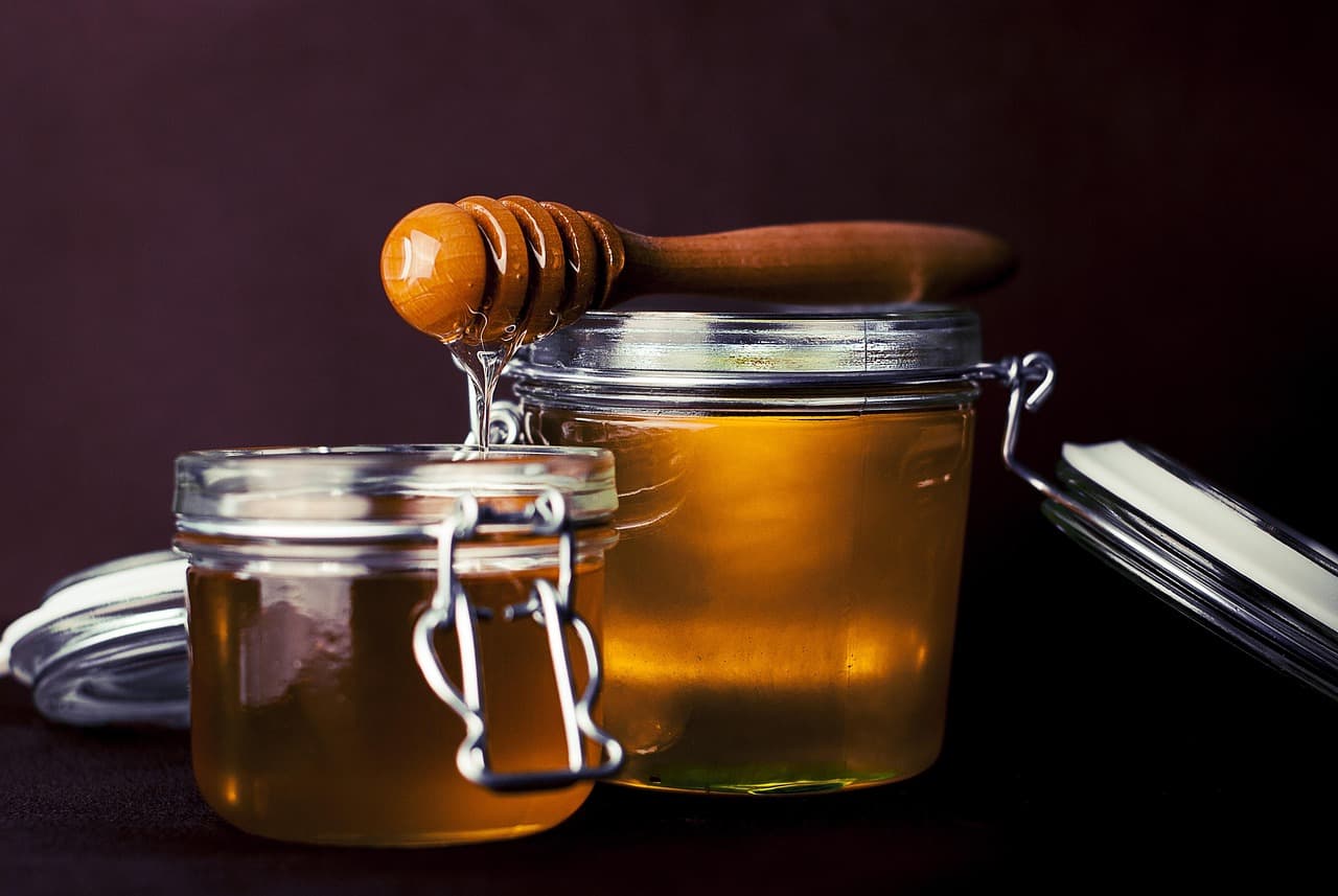 Honey being drizzled from a wooden dipper into glass jars